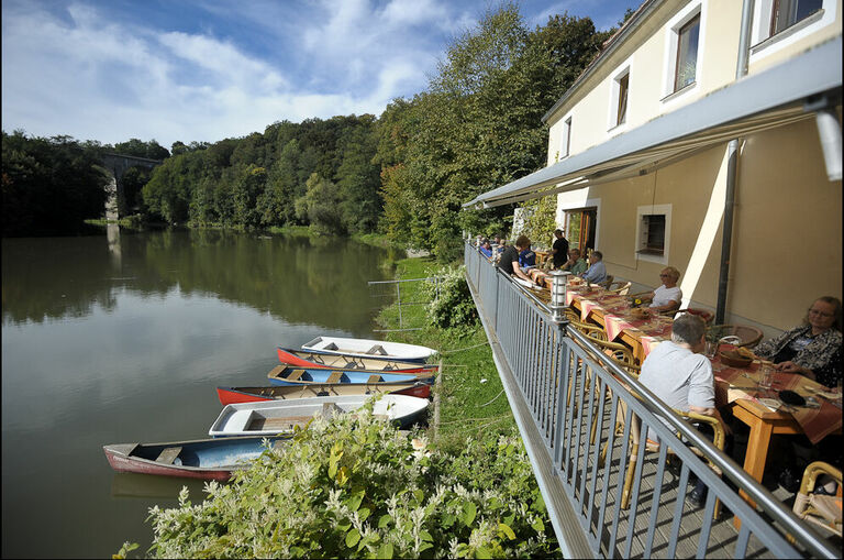 Der Außenbereich der Obermühle Görlitz: Gäste sitzen hier am Ufer der Neisse, an dem einige Ruderboote liegen.