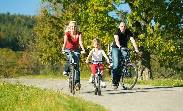 Eine Familie fährt bei sonnigem Wetter mit dem Fahrrad durch die Landschaft.