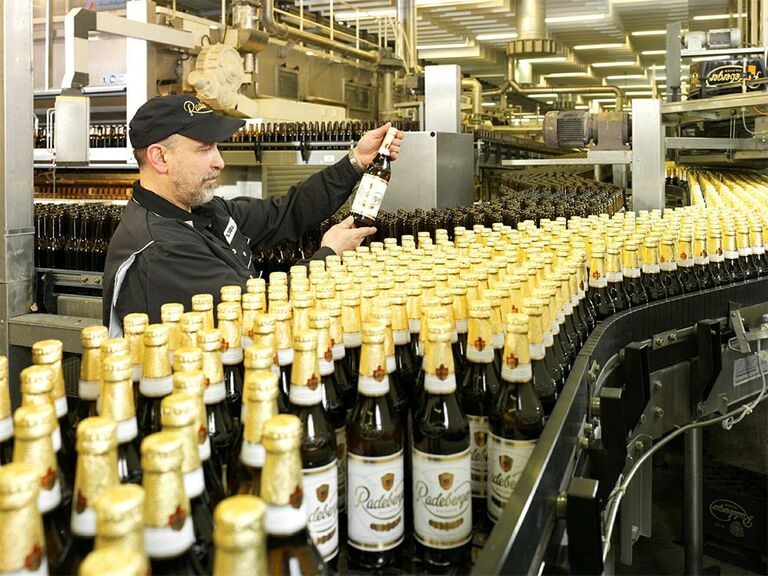Ein Mann überprüft das Aussehen des Bieres auf der Produktionsstraße in der Radeberger Brauerei. Im Vordergrund gehen unzählige Flaschen über das Produktionsband.