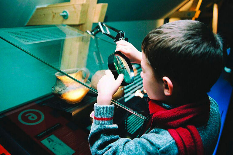 Ein Kind betrachtet mit Lupe die Exponate im Museum der Westlausitz.