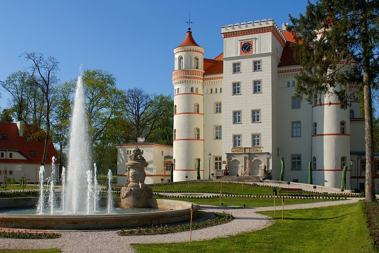 Blick auf das Schloss Wojanow mit dem Brunnen im Vordergrund.