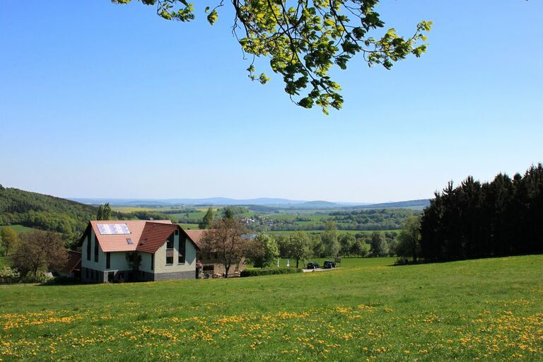 Die Rote Schenke hinter einer Wiese und vor einem weiten Ausblick von weitem betrachtet.